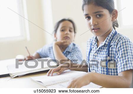 Stock Image - Portrait of a schoolgirl sitting at a desk with her friend sitting beside her. Fotosearch
