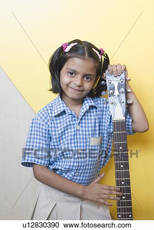 Stock Image - Portrait of a schoolgirl standing with a guitar and smiling. Fotosearch