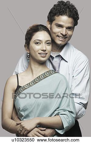 Stock Image - Portrait of a young man embracing a young woman from behind. Fotosearch
