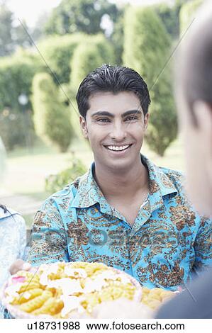 Stock Photo - Portrait of a young man holding a dish of Indian sweets smiling. Fotosearch