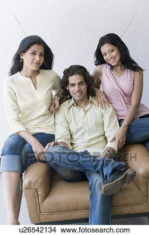 Picture - Portrait of a young man sitting between two young women and smiling. Fotosearch