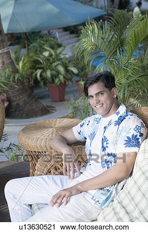 Portrait of a young man sitting on a couch and smiling View Large Photo Image Stock Image - Portrait of a young man sitting on a couch and smiling. Fotosearch