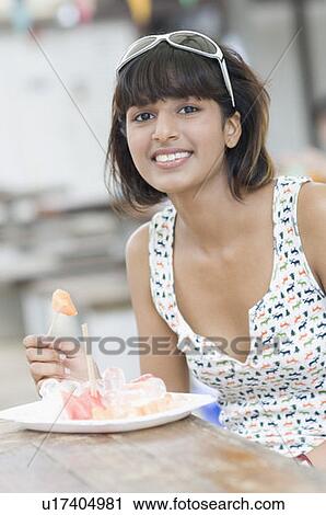 Stock Image - Portrait of a young woman eating fruit salad and smiling. Fotosearch
