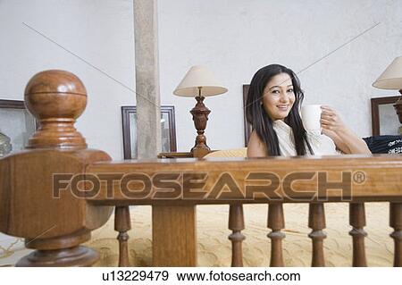 Stock Photo - Portrait of a young woman holding a coffee cup and smiling. Fotosearch