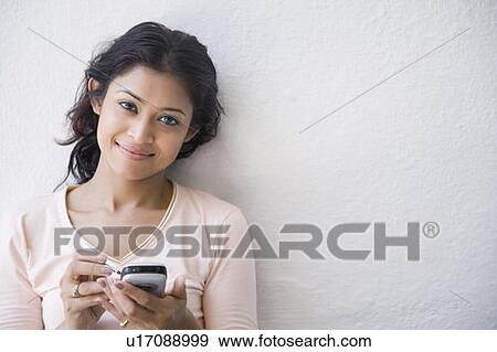 Stock Photo - Portrait of a young woman holding a mobile phone and smiling. Fotosearch