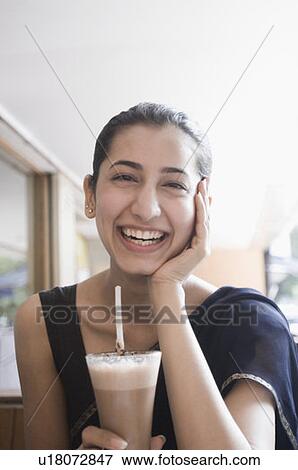 Stock Photo - Portrait of a young woman holding a glass of chocolate milkshake and smiling. Fotosearch