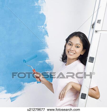 Portrait of a young woman holding a paint roller and smiling View Large Photo Image Stock Photo - Portrait of a young woman holding a paint roller and smiling. Fotosearch