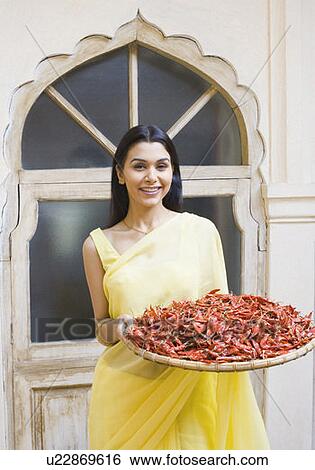 Stock Photograph - Portrait of a young woman holding a basket of red chili pepper and smiling. Fotosearch