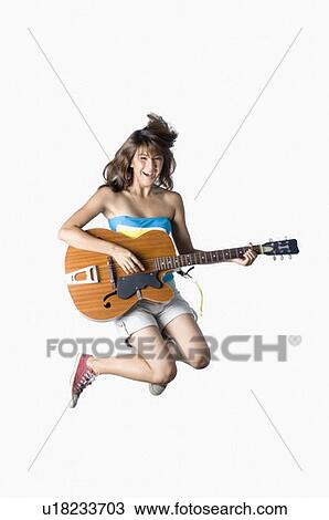 Stock Image - Portrait of a young woman jumping and playing a guitar. Fotosearch