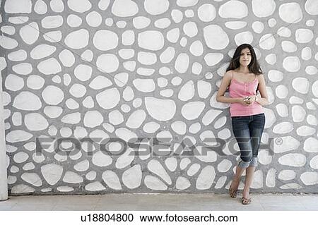 Portrait of a young woman leaning against a wall and holding a mobile phone View Large Photo Image Stock Image - Portrait of a young woman leaning against a wall and holding a mobile phone. Fotosearch
