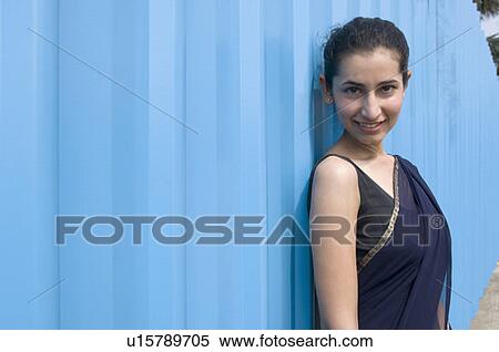 Stock Photography - Portrait of a young woman leaning against a wall and smiling. Fotosearch