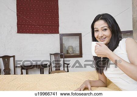 Portrait of a young woman lying on the bed with holding a coffee cup View Large Photo Image Stock Image - Portrait of a young woman lying on the bed with holding a coffee cup. Fotosearch