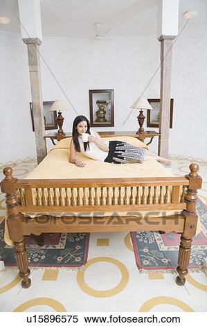 Stock Photography - Portrait of a young woman lying on the bed with holding a coffee cup. Fotosearch