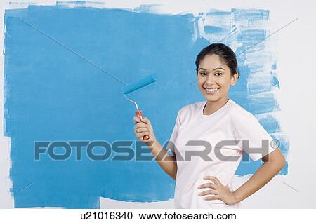 Stock Image - Portrait of a young woman painting a wall and smiling. Fotosearch