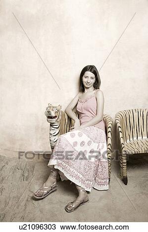 Portrait of a young woman sitting on a chair and grinning View Large Photo Image Stock Image - Portrait of a young woman sitting on a chair and grinning. Fotosearch