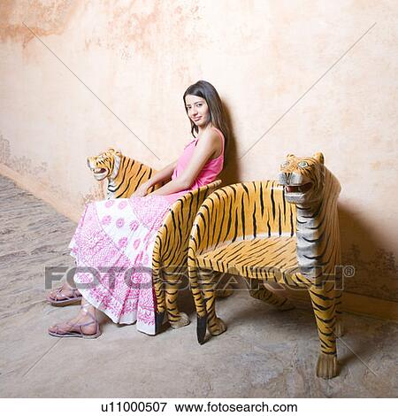 Stock Photo - Portrait of a young woman sitting on a chair and smirking. Fotosearch