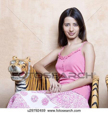 Portrait of a young woman sitting on a chair View Large Photo Image Stock Photo - Portrait of a young woman sitting on a chair. Fotosearch