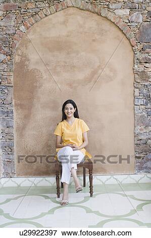 Portrait of a young woman sitting on a chair and smiling View Large Photo Image Stock Photo - Portrait of a young woman sitting on a chair and smiling. Fotosearch