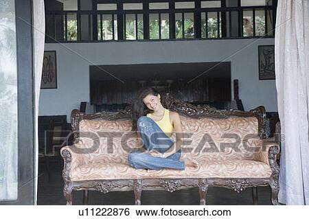 Portrait of a young woman sitting on a couch and smiling View Large Photo Image Stock Photograph - Portrait of a young woman sitting on a couch and smiling. Fotosearch