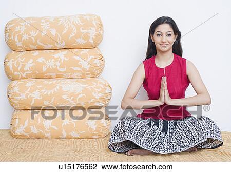 Stock Image - Portrait of a young woman sitting on the bed beside a stack of cushions. Fotosearch