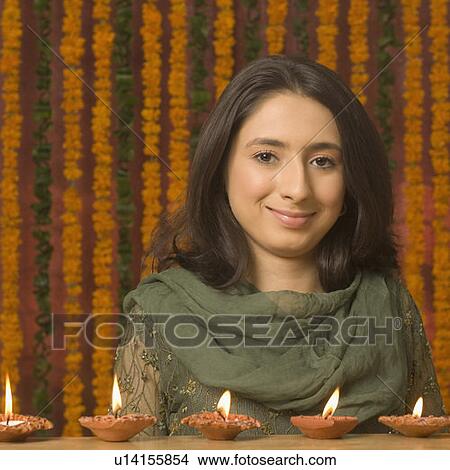 Picture - Portrait of a young woman smirking with oil lamps in front of her. Fotosearch