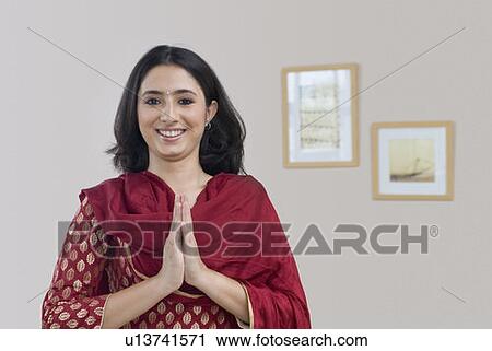 Stock Image - Portrait of a young woman standing in prayer position and smiling. Fotosearch