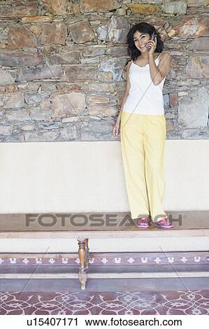 Stock Image - Portrait of a young woman standing on a bench and talking on a mobile phone. Fotosearch