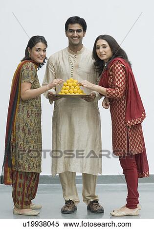 Portrait of two young women standing with a young man holding a plate of laddoos View Large Photo Image Stock Photography - Portrait of two young women standing with a young man holding a plate of laddoos. Fotosearch