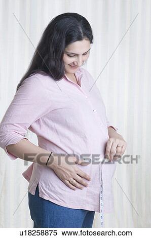 Stock Photography - Pregnant woman measuring her abdomen with a tape measure. Fotosearch