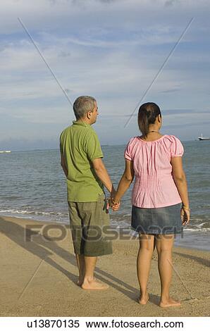 Rear view of a mid adult couple holding hands of each other on the beach View Large Photo Image Stock Photography - Rear view of a mid adult couple holding hands of each other on the beach. Fotosearch