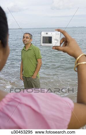 Rear view of a mid adult woman taking a photograph of a mid adult man on the beach View Large Photo Image Stock Photography - Rear view of a mid adult woman taking a photograph of a mid adult man on the beach. Fotosearch
