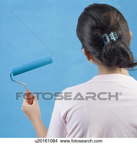 Rear view of a young woman painting a wall with a paint roller View Large Photo Image Picture - Rear view of a young woman painting a wall with a paint roller. Fotosearch