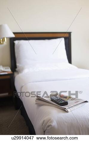 Remote control and a newspaper on the bed in a hotel room View Large Photo Image Stock Photo - Remote control and a newspaper on the bed in a hotel room. Fotosearch