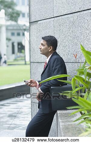 Stock Photo - Side profile of a businessman holding a mobile phone. Fotosearch