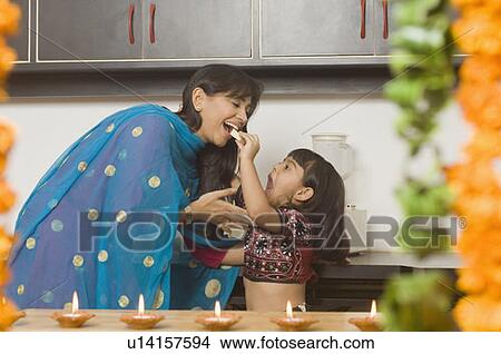 Side profile of a girl feeding a piece of burfi to her mother in a domestic kitchen View Large Photo Image Picture - Side profile of a girl feeding a piece of burfi to her mother in a domestic kitchen. Fotosearch