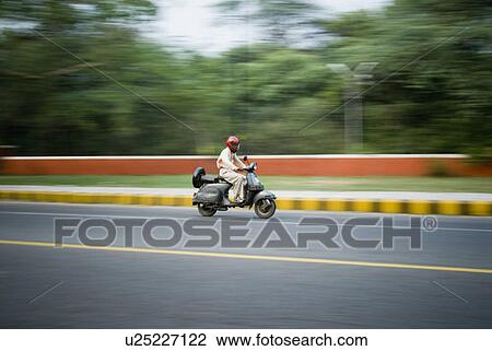 Stock Image - Side profile of a man riding a scooter, New Delhi, India. Fotosearch