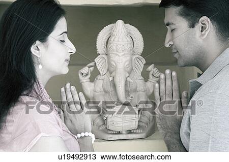 Side profile of a mid adult couple praying in front of a statue of God Ganesha View Large Photo Image Stock Image - Side profile of a mid adult couple praying in front of a statue of God Ganesha. Fotosearch