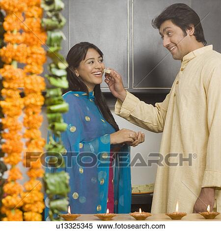 Side profile of a mid adult man feeding a piece of burfi to a young woman in a domestic kitchen and smiling View Large Photo Image Stock Photography - Side profile of a mid adult man feeding a piece of burfi to a young woman in a domestic kitchen and smiling. Fotosearch