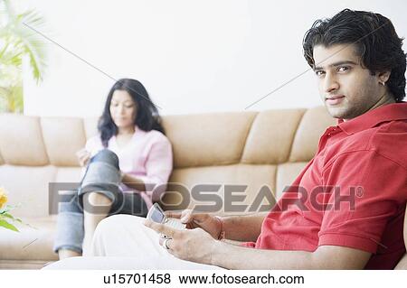 Stock Photo - Side profile of a young man holding a mobile phone with a young woman sitting beside him. Fotosearch