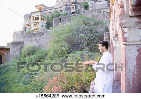 Stock Photograph - Side profile of a young man holding a plate of powder paint and standing at the balcony of a fort, Neemrana Fort Palace, Neemrana, Alwar, Rajasthan, India. Fotosearch