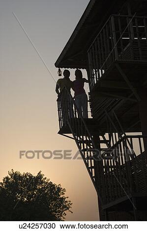 Stock Image - Silhouette of a young couple standing on the beach hut. Fotosearch
