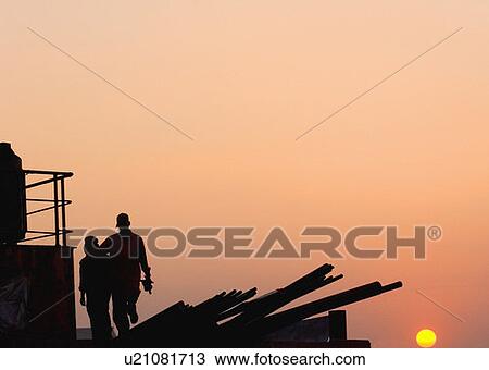 Stock Image - Silhouette of two workers at a Dock, Shipping Yard, Mumbai, Maharashtra, India. Fotosearch