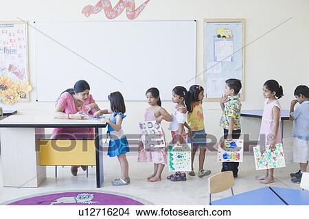 Teacher checking drawings of students in a classroom View Large Photo Image Picture - Teacher checking drawings of students in a classroom. Fotosearch