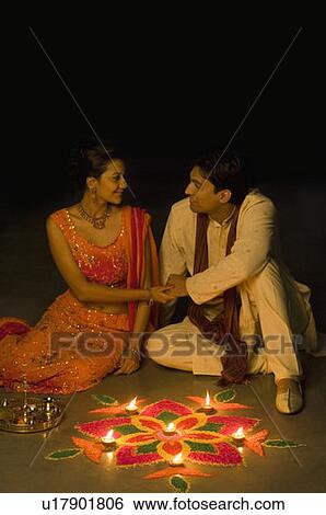 Stock Photograph - Young couple sitting with holding hands in front of rangoli. Fotosearch