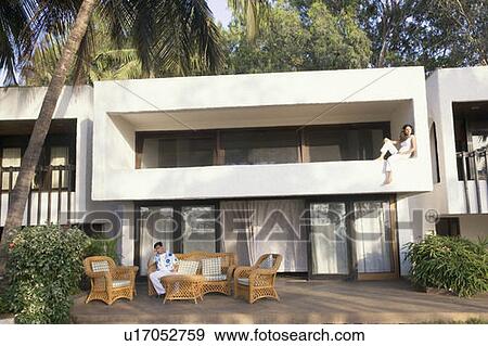 Stock Photo - Young man sitting on a couch with a young woman sitting on a porch behind him. Fotosearch