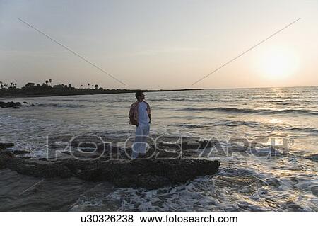 Young man standing on the coast with his hands in his pockets View Large Photo Image Stock Photo - Young man standing on the coast with his hands in his pockets. Fotosearch