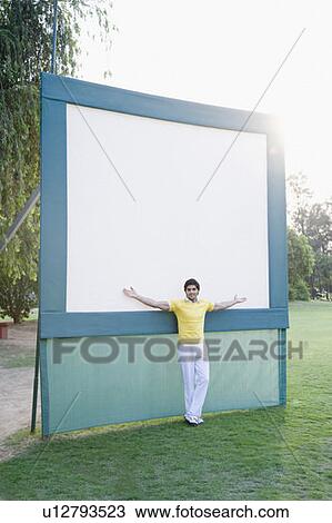 Stock Image - Young man standing with his arms outstretched in front of a visual screen. Fotosearch