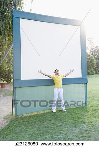 Stock Image - Young man standing with his arms outstretched in front of a whiteboard. Fotosearch