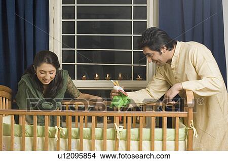Young woman and a mid adult man looking inside a crib and smiling View Large Photo Image Picture - Young woman and a mid adult man looking inside a crib and smiling. Fotosearch