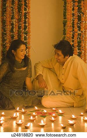 Stock Image - Young woman and a mid adult man sitting behind traditional diwali lamps. Fotosearch